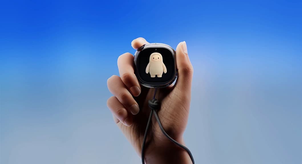Hand holding a small black device with a white character on the screen, against a light blue background.